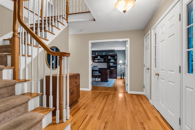 entrance foyer with light wood-type flooring, baseboards, and stairs