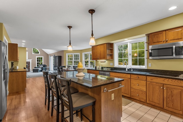 kitchen with a breakfast bar area, a sink, open floor plan, appliances with stainless steel finishes, and brown cabinets