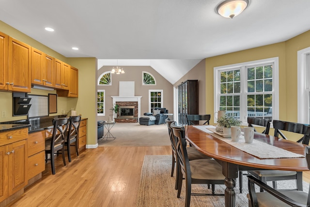 dining area featuring lofted ceiling, a fireplace, light wood-style floors, and a wealth of natural light