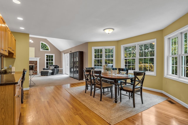 dining area with light wood-type flooring, visible vents, lofted ceiling, baseboards, and a brick fireplace