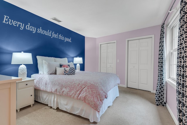 bedroom with multiple windows, visible vents, two closets, and light carpet