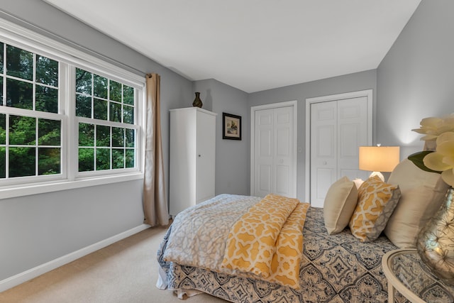 carpeted bedroom featuring baseboards and two closets