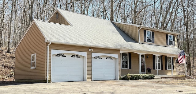 view of front facade with covered porch, driveway, a shingled roof, and a garage