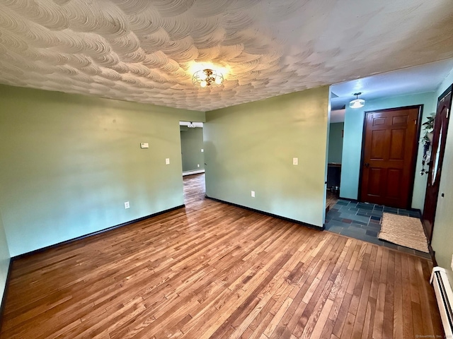 unfurnished room featuring a baseboard heating unit, a baseboard radiator, hardwood / wood-style flooring, and baseboards