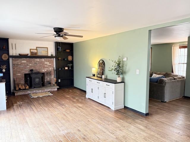 living room featuring a ceiling fan, a wood stove, baseboards, and wood finished floors