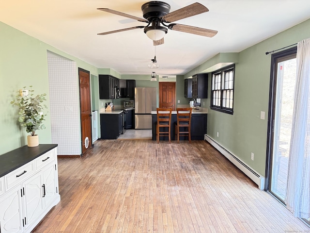 kitchen featuring ceiling fan, freestanding refrigerator, baseboard heating, dark cabinetry, and light wood-style floors