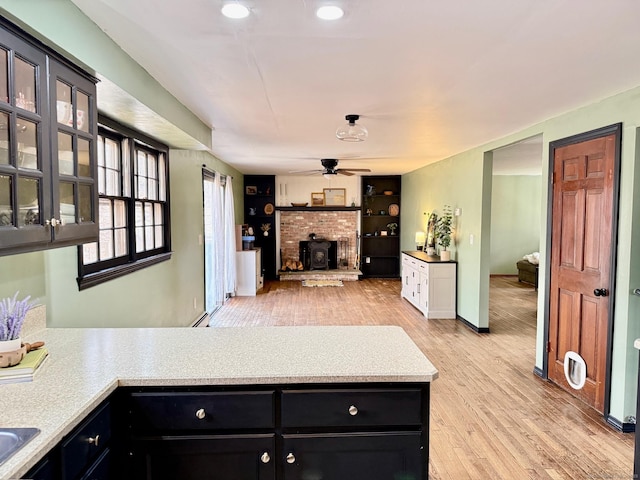 kitchen featuring glass insert cabinets, dark cabinets, a peninsula, light countertops, and light wood-type flooring