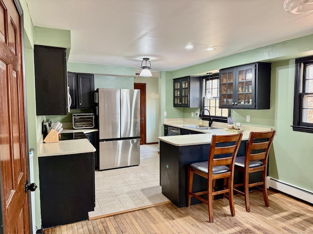 kitchen with dark cabinets, stainless steel appliances, a peninsula, a sink, and light countertops