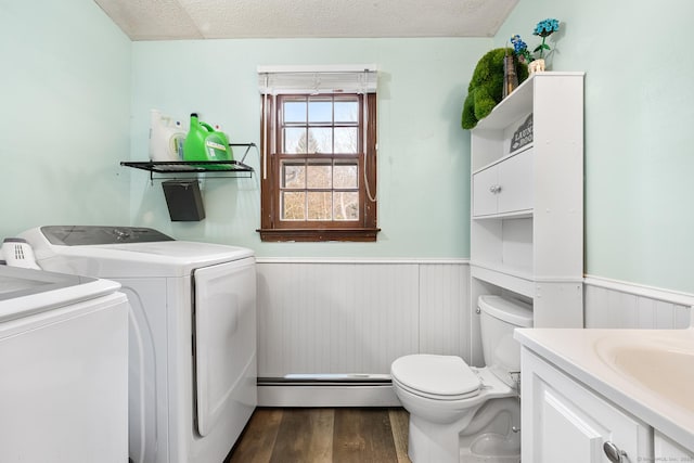 laundry area with laundry area, washer and clothes dryer, a wainscoted wall, dark wood-style flooring, and a baseboard heating unit