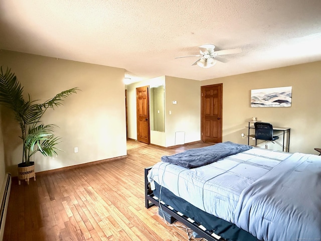 bedroom featuring a baseboard heating unit, baseboards, a textured ceiling, and light wood finished floors