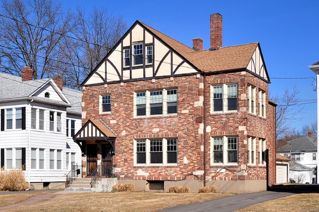 rear view of house featuring an outbuilding, brick siding, roof with shingles, and a chimney