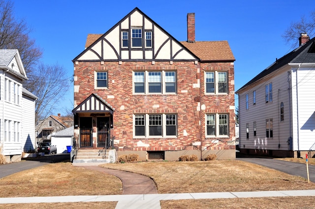 view of front of home with driveway, stucco siding, a chimney, a shingled roof, and brick siding