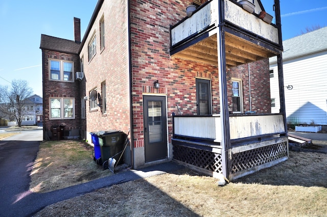 back of property featuring brick siding, a chimney, and a balcony