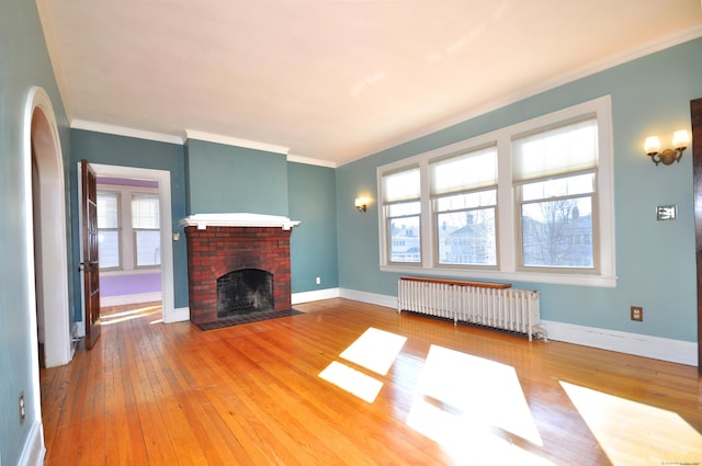 unfurnished living room featuring hardwood / wood-style floors, a brick fireplace, radiator heating unit, and plenty of natural light