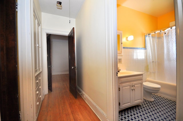 bathroom featuring toilet, shower / tub combo with curtain, vanity, wood finished floors, and tile walls