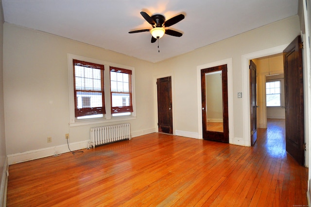 unfurnished room with ceiling fan, baseboards, radiator heating unit, and light wood-style floors