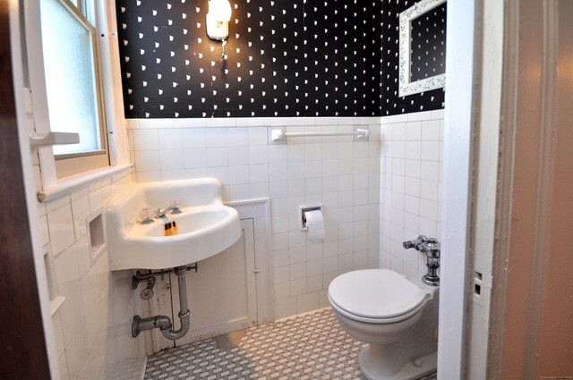 half bathroom featuring wallpapered walls, tile walls, toilet, and wainscoting