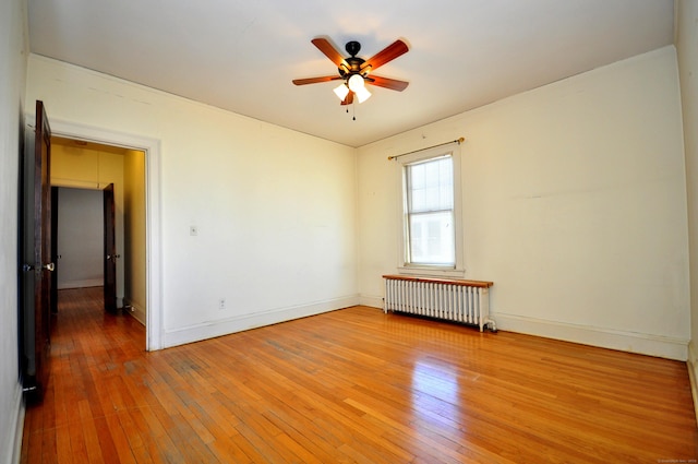 unfurnished room featuring baseboards, light wood-style floors, ceiling fan, and radiator heating unit