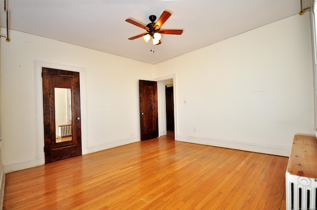 unfurnished room featuring baseboards, a ceiling fan, light wood-style flooring, and radiator heating unit