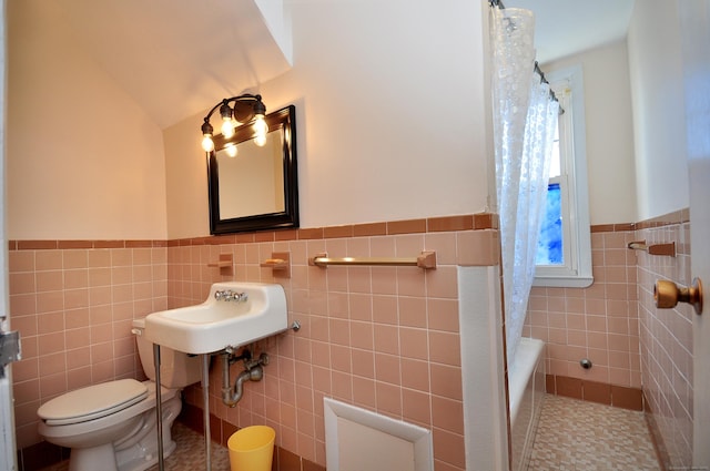 bathroom featuring toilet, wainscoting, a shower with curtain, tile walls, and a sink