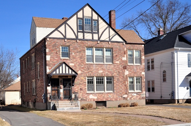 english style home with stucco siding, a chimney, brick siding, and a shingled roof