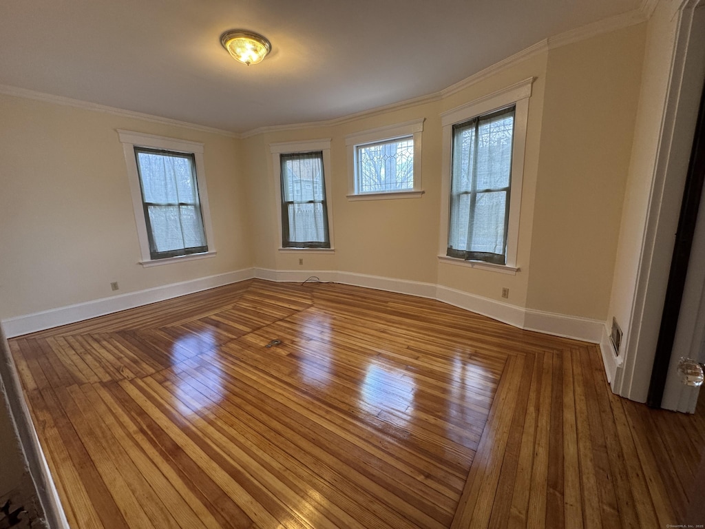 unfurnished room with crown molding, wood-type flooring, baseboards, and a healthy amount of sunlight