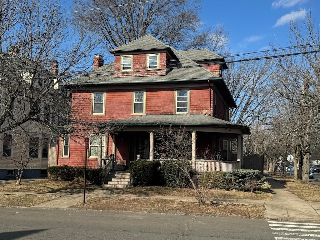 traditional style home featuring covered porch, a shingled roof, and a chimney