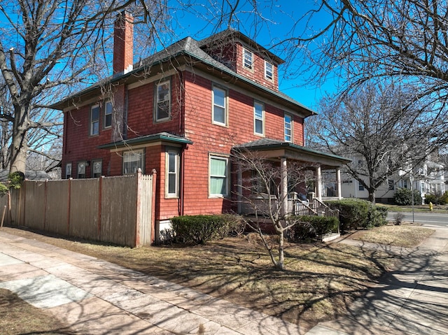 view of home's exterior featuring covered porch, a chimney, and fence