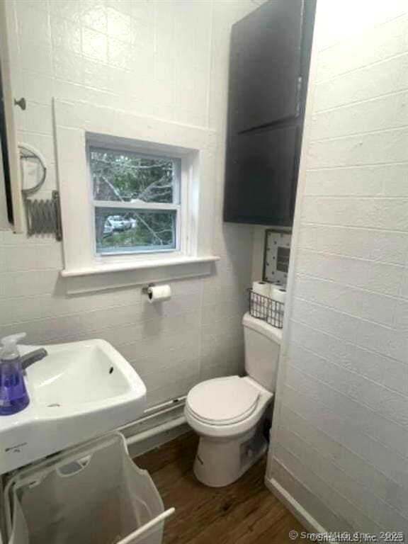 half bathroom with tile walls, toilet, wood finished floors, and a sink