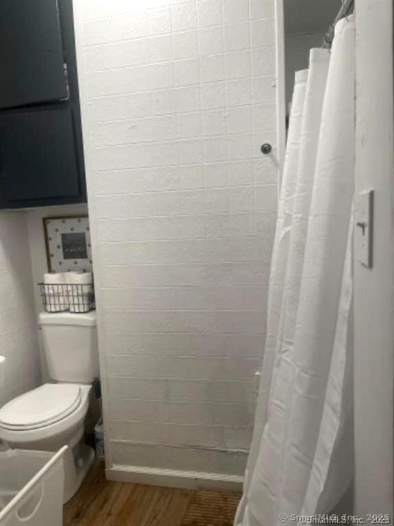 bathroom with tiled shower, toilet, and wood finished floors