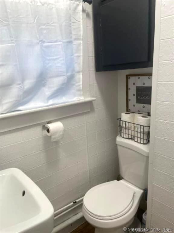 bathroom with toilet and tile walls