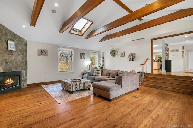 living area featuring lofted ceiling with skylight, visible vents, a stone fireplace, and light wood-style floors