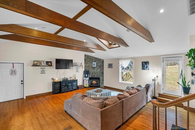 living room featuring baseboards, light wood-type flooring, vaulted ceiling with skylight, and a stone fireplace