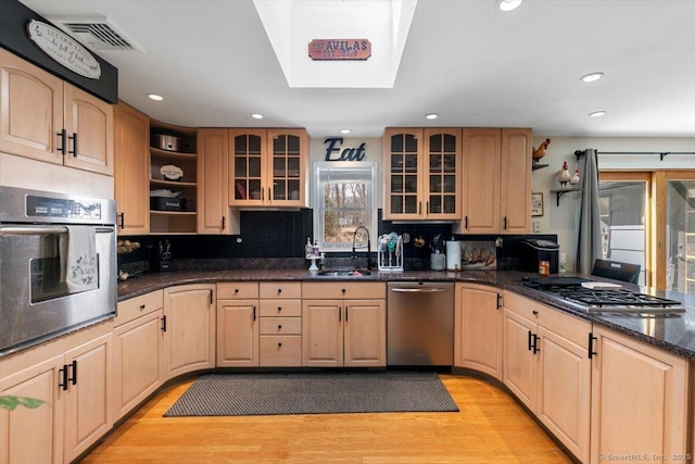 kitchen with visible vents, a peninsula, light brown cabinetry, a sink, and appliances with stainless steel finishes