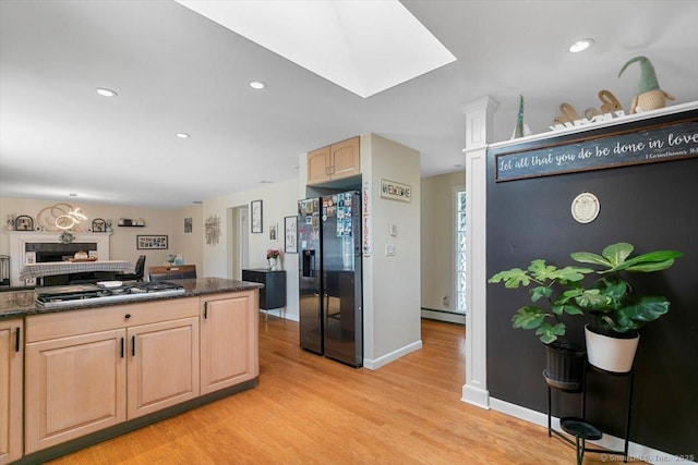 kitchen featuring light brown cabinets, stainless steel gas cooktop, light wood-style flooring, baseboard heating, and black fridge