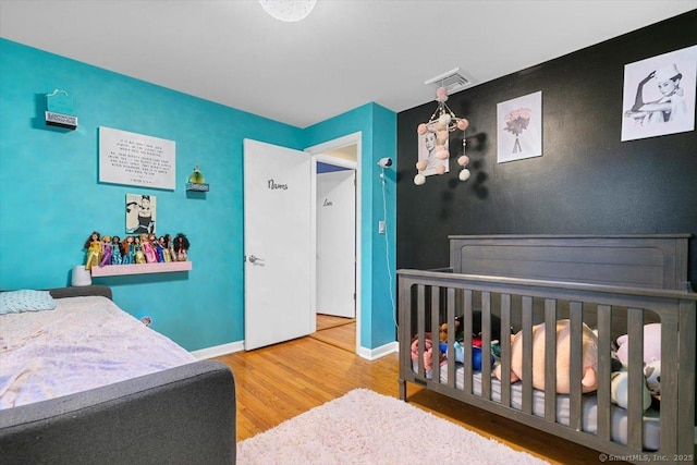 bedroom featuring visible vents, an accent wall, baseboards, and wood finished floors