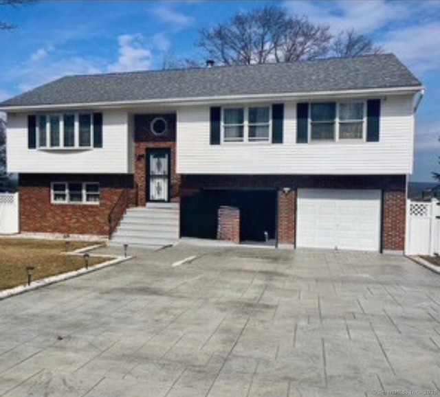 bi-level home featuring brick siding, driveway, and fence