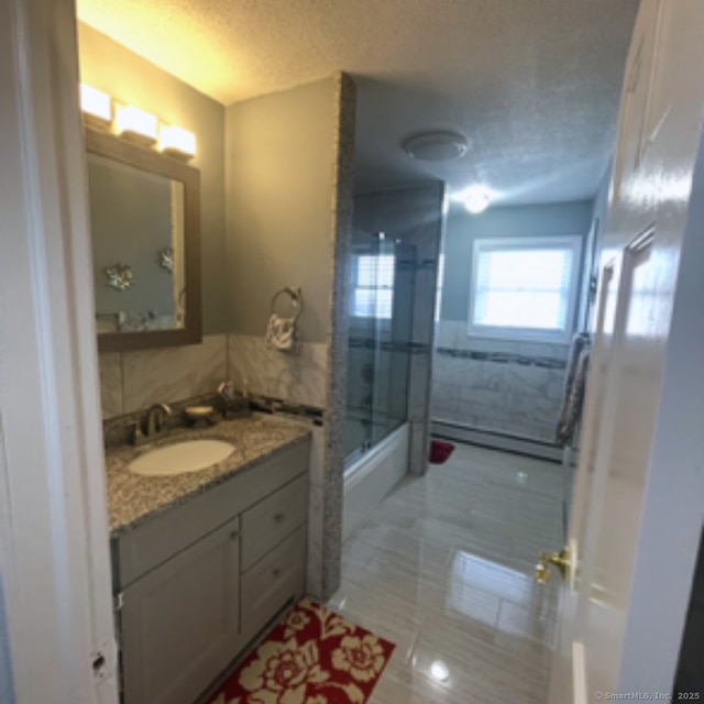 full bath featuring vanity, tile walls, bath / shower combo with glass door, and a textured ceiling