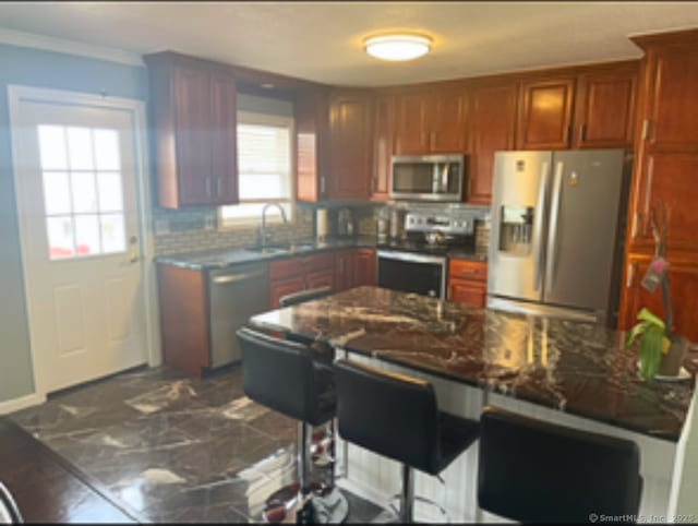 kitchen with a kitchen bar, a sink, tasteful backsplash, stainless steel appliances, and crown molding