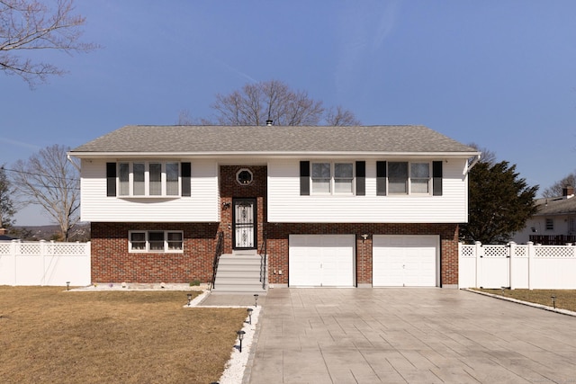 bi-level home with a front lawn, fence, concrete driveway, an attached garage, and brick siding