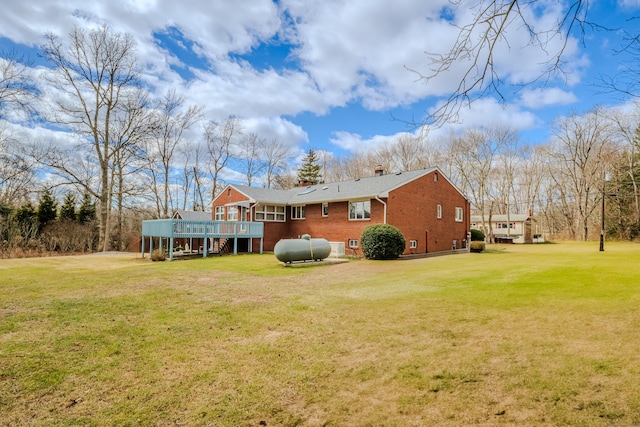 rear view of property with a yard, a chimney, brick siding, and a wooden deck