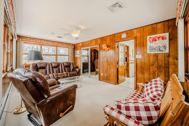 living area with wooden walls, ceiling fan, light colored carpet, and visible vents