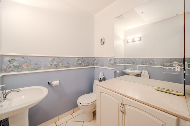half bathroom featuring tile patterned flooring, a sink, wainscoting, and toilet