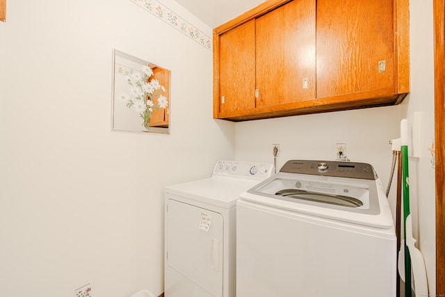 clothes washing area with separate washer and dryer and cabinet space