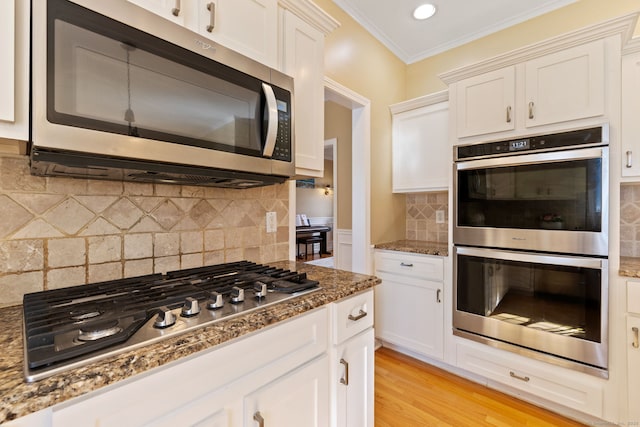 kitchen with light wood-style flooring, stone countertops, white cabinets, appliances with stainless steel finishes, and crown molding