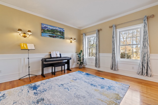 sitting room with crown molding, wood finished floors, visible vents, and a wainscoted wall