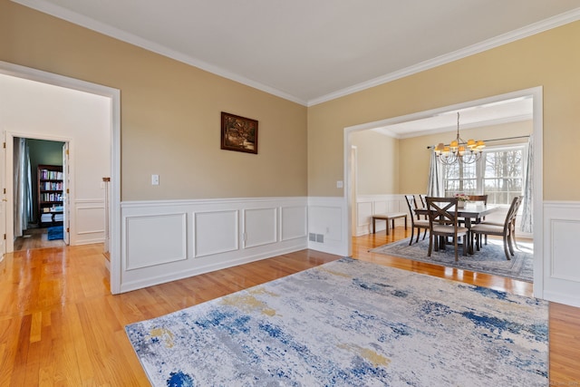 dining area with light wood finished floors, visible vents, a chandelier, ornamental molding, and wainscoting