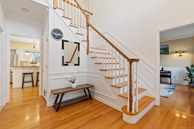 stairs with a decorative wall, crown molding, a wainscoted wall, and wood finished floors