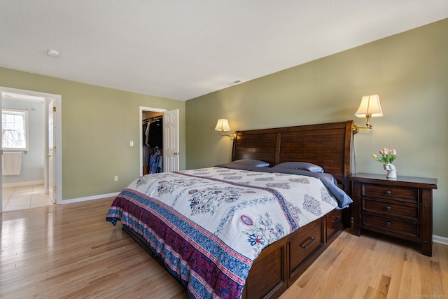 bedroom featuring light wood finished floors, visible vents, a walk in closet, baseboards, and a closet