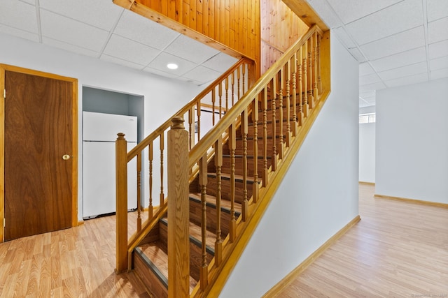 staircase with a paneled ceiling, baseboards, and wood finished floors